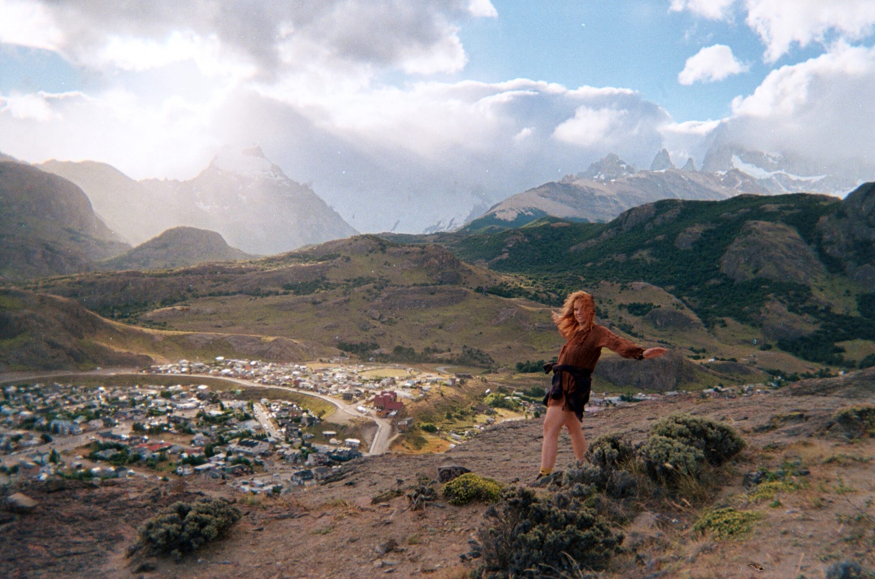 Frida en una ladera de El Chaltén con el cordón Fitz Roy detrás, el pelo al viento y los brazos abiertos